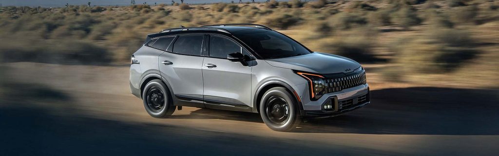 Silver Kia Sportage SUV driving on a dusty desert road with blurred background vegetation and motion effect.