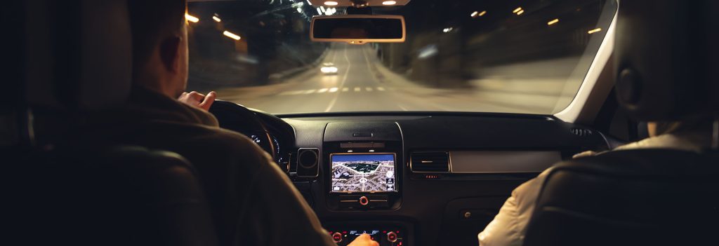 A person driving a car at night with a GPS navigation screen visible.