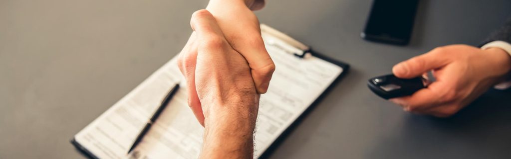 Two people shaking hands with a car key and document on the table.