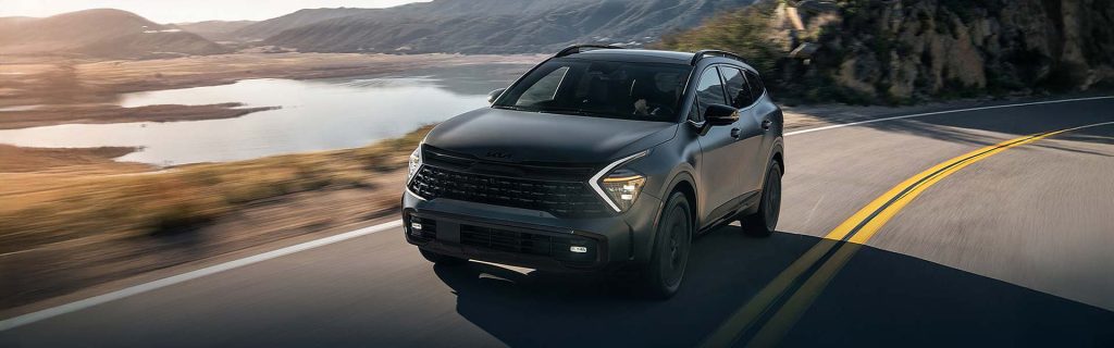 Black SUV driving on a winding mountain road beside a lake.